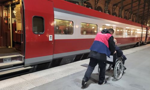 Personnel en gare poussant un passager en fauteuil roulant sur un quai.