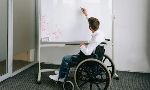 Un homme en fauteuil roulant écrit sur un tableau blanc.
