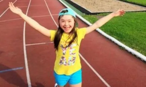 Une jeune fille avec trisomie, très souriante, court sur une piste d’athlétisme.
