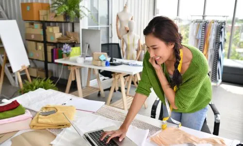 Une jeune femme souriante, au téléphone, est sur son ordinateur.