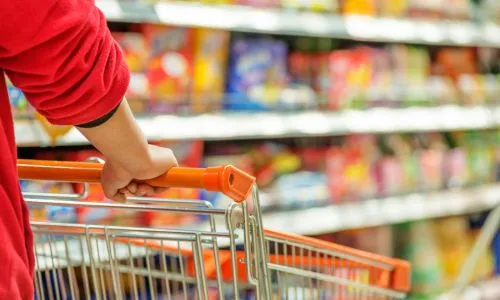 Zoom sur les mains d’une femme qui pousse un chariot dans un supermarché.