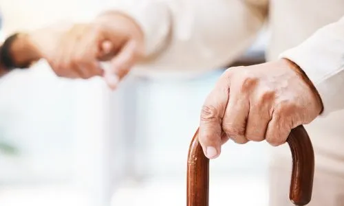 Une aide à domicile tient la main d’une femme avec une canne.