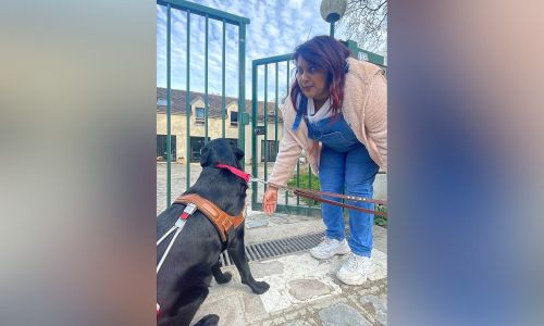 Un chien guide labrador noir et son maître devant l’école à Paris.